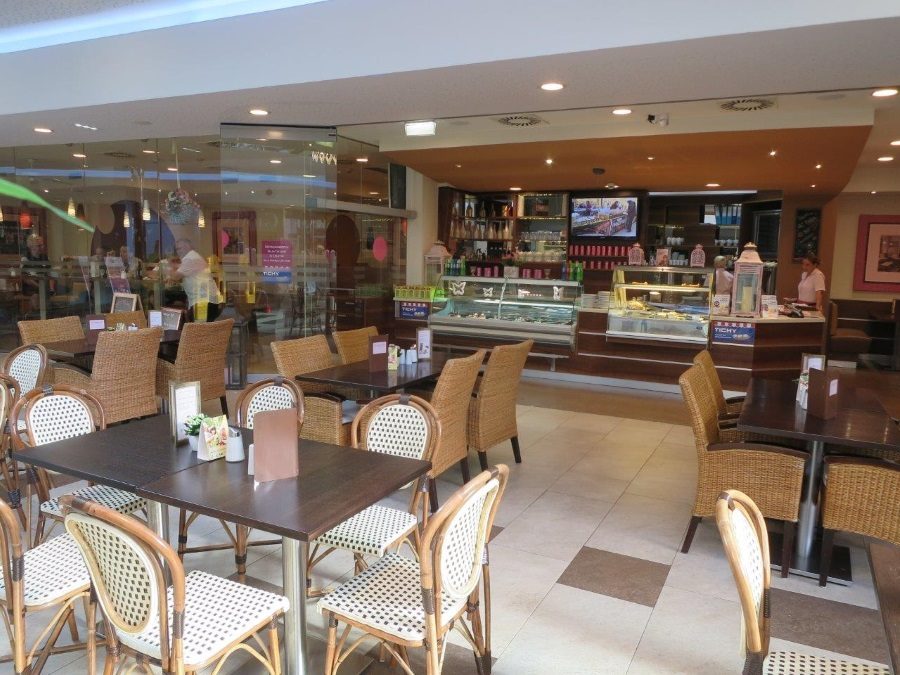 Gastraum der Café Konditorei Schickh mit Tischen, Korbstühlen und beleuchteter Kuchenvitrine