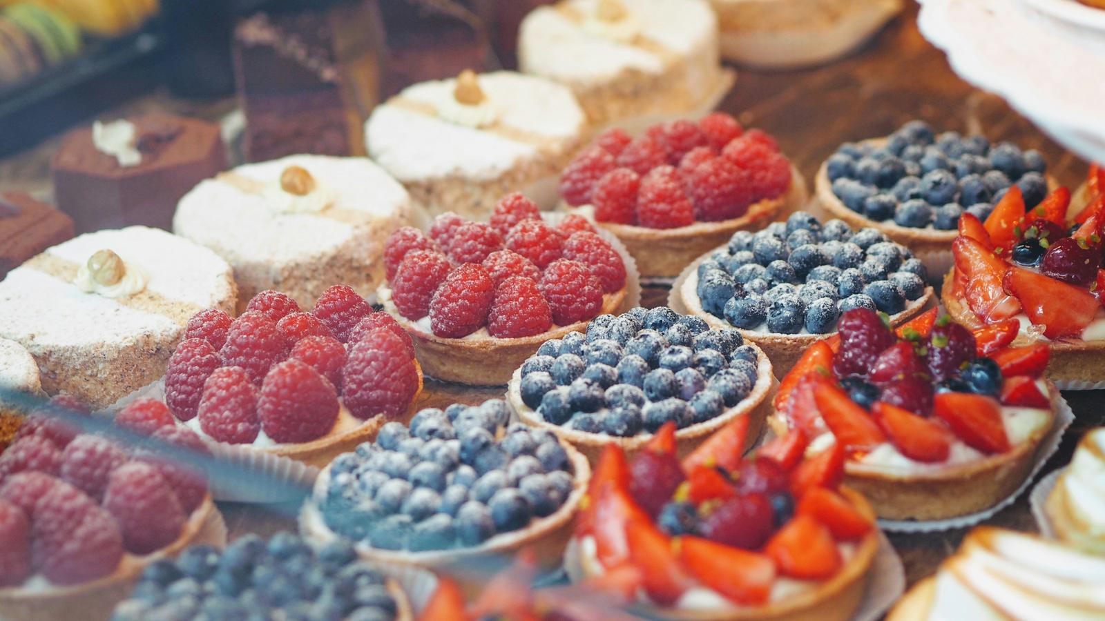 Vitrine voller Fruchttartelettes mit Himbeeren, Heidelbeeren und Erdbeeren, dahinter feine Törtchen mit Haselnuss