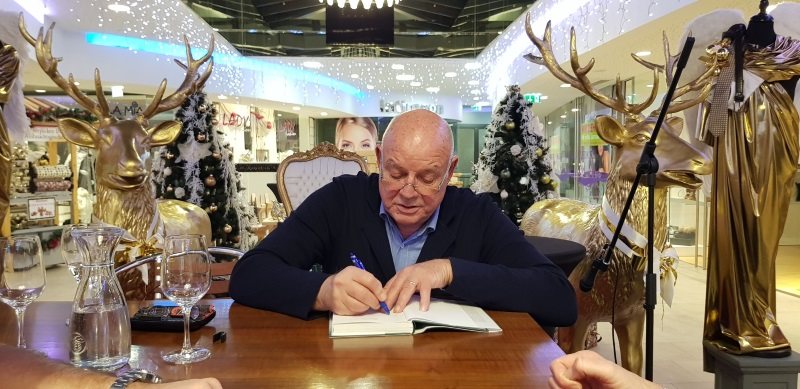 Wolfgang Böck signiert bei seiner Lesung „Habt’s mich gern“ in der weihnachtlich dekorierten Passage ein Buch